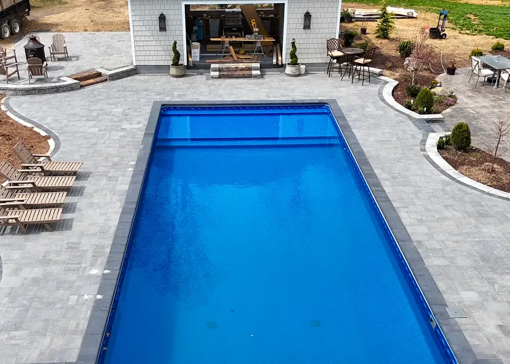 Blue rectangular vinyl liner pool with a stone deck and spa